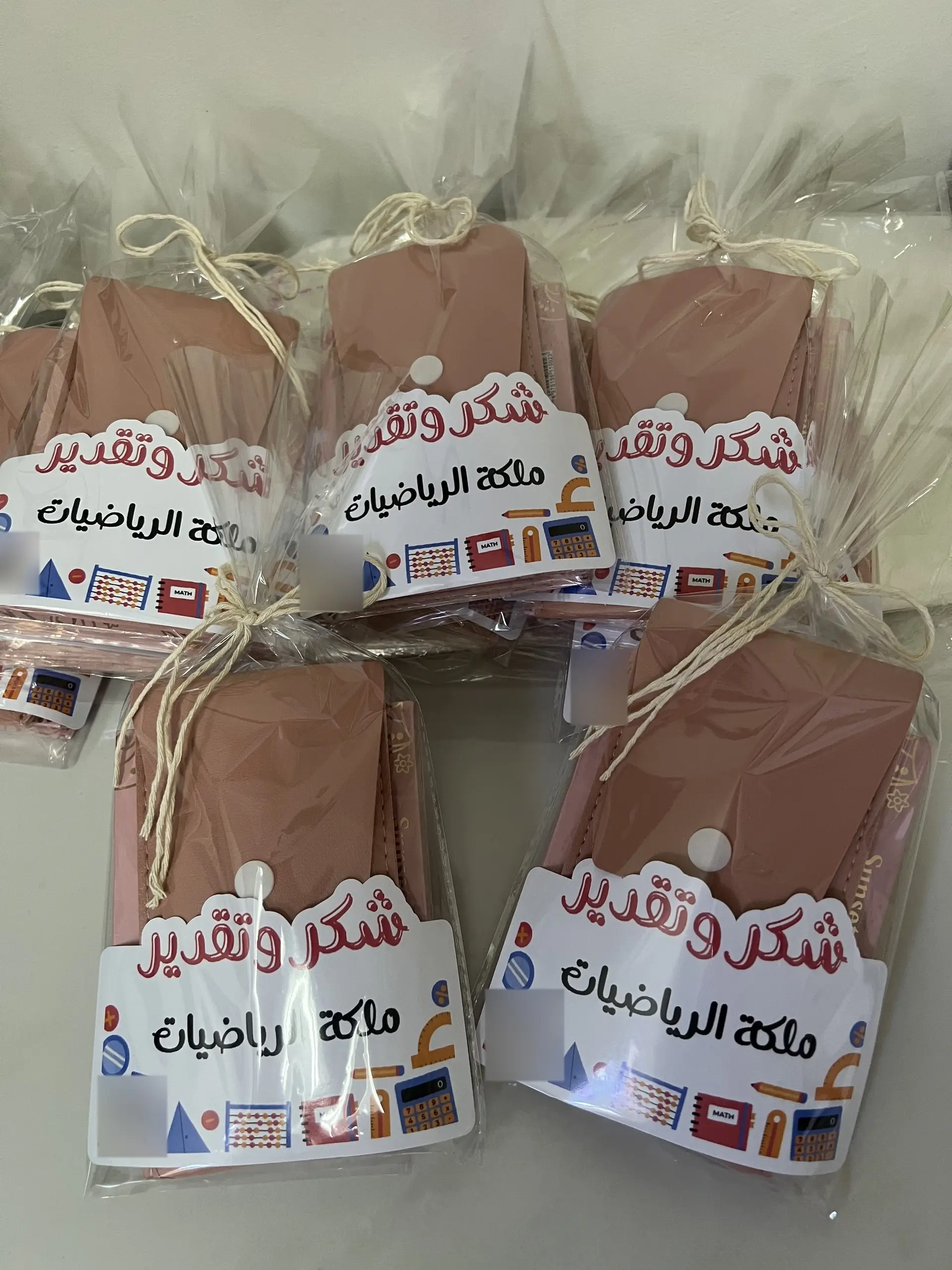 حافظة وردية في كيس شفاف، أمامها بطاقة «شكر وتقدير» برسوم أدوات الرياضيات.
